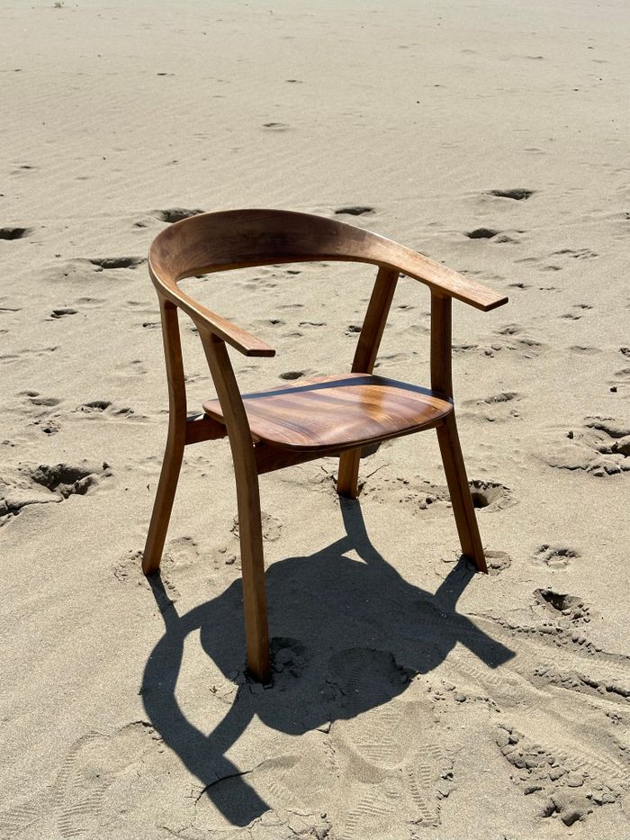A wooden chair casting shadow on a sandy beach, highlighting solitude and simplicity.