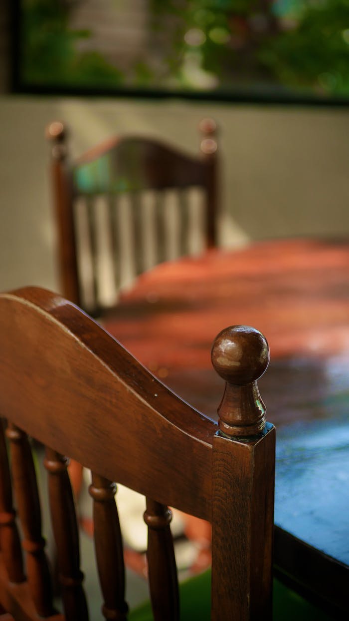 Close-up of wooden dining chairs with sunlight through window, creating a cozy ambiance.