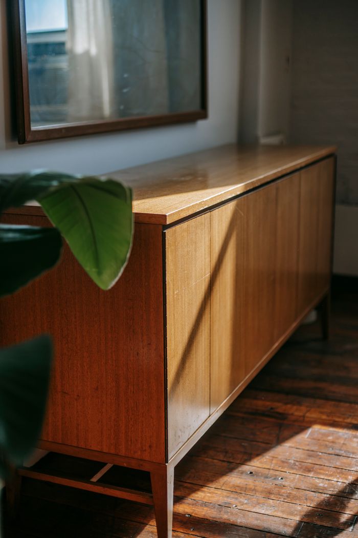 Rectangular shaped desk under mirror reflecting window near plant leaves at home in sunlight