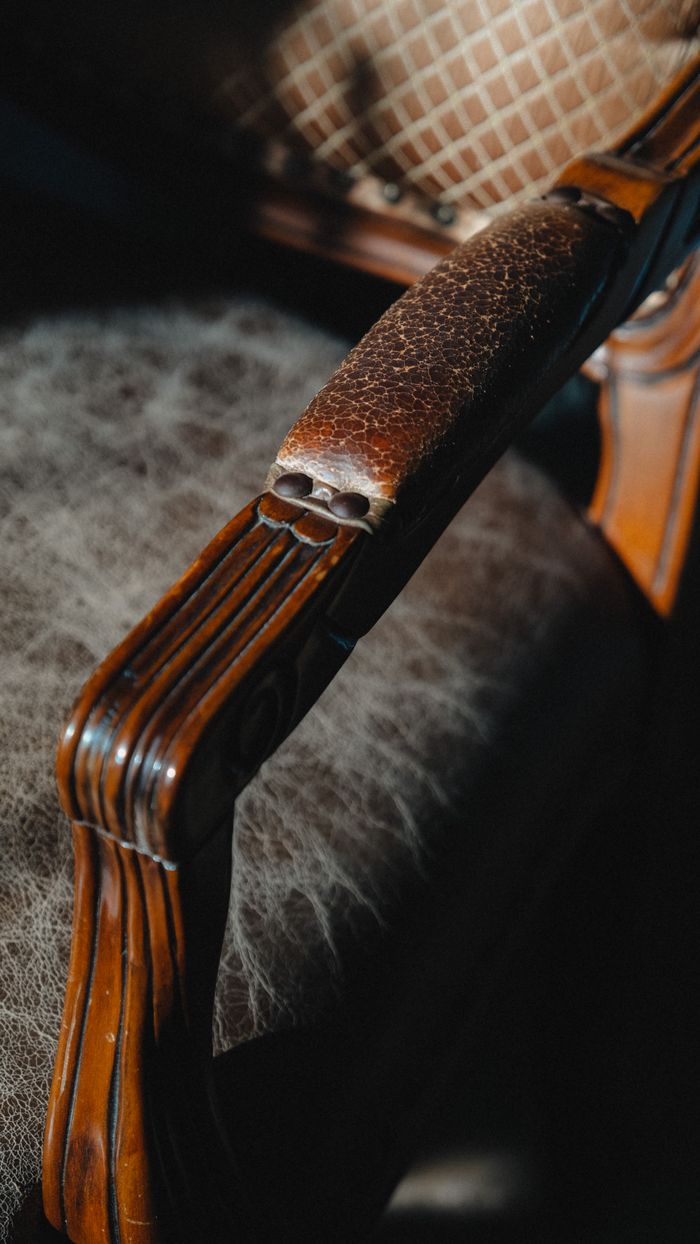 Detailed shot of a classic wooden armchair with leather armrest, showcasing retro style.